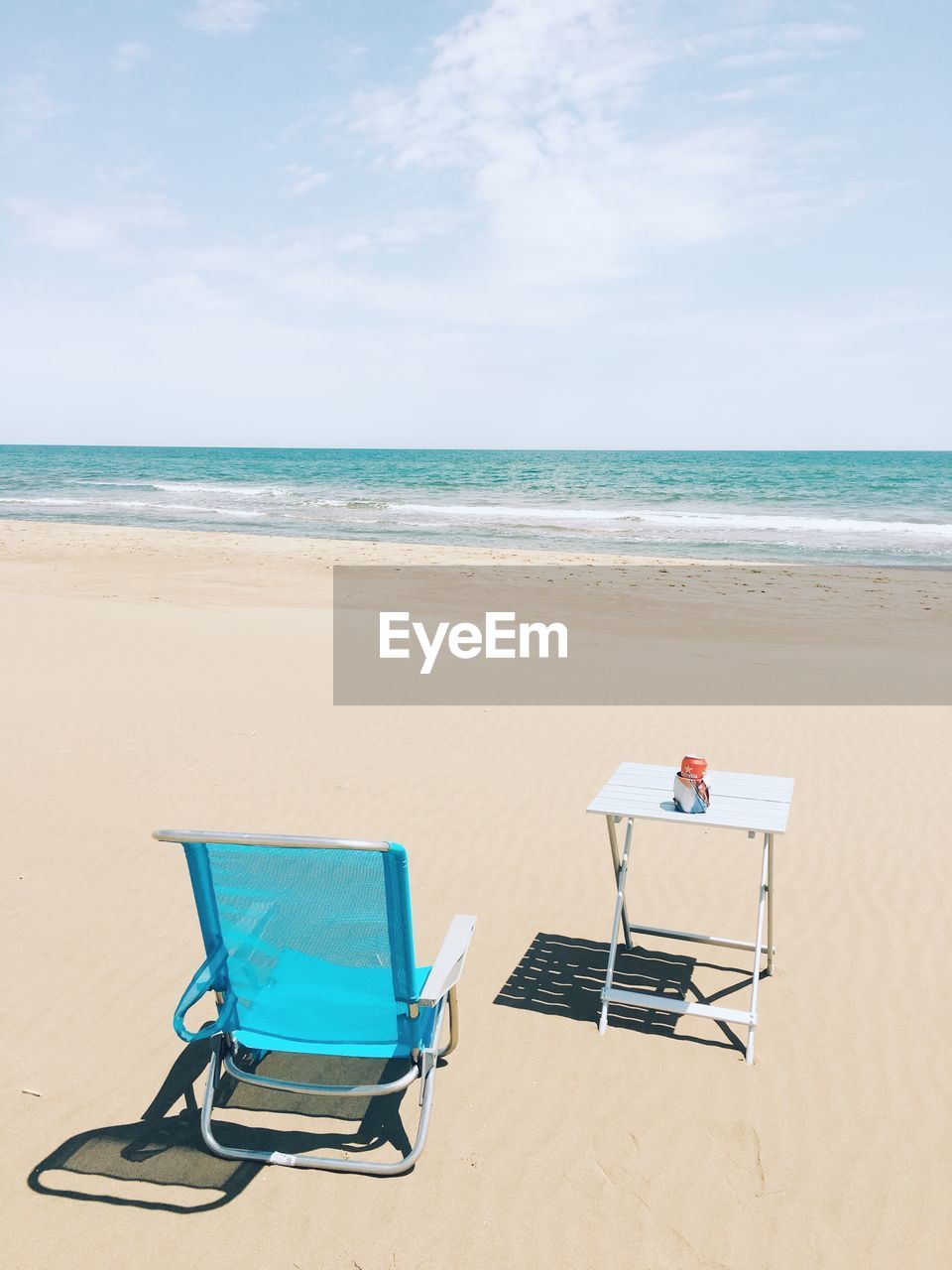 Deck chair and table on beach against sky