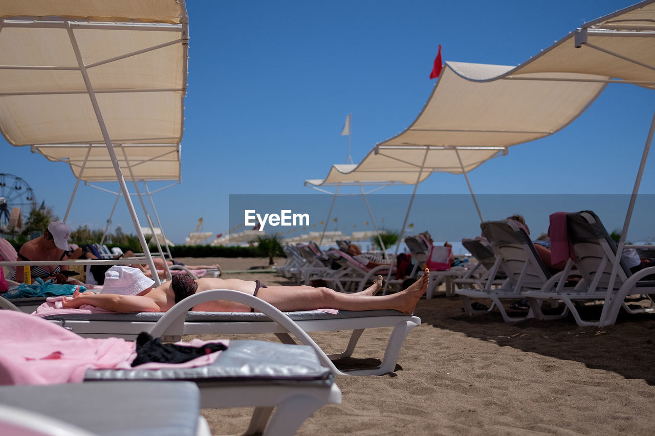 Woman relaxing on lounge chair at beach against sky