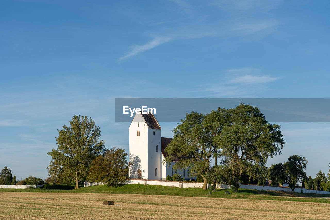 sky, plant, architecture, built structure, tree, rural area, building exterior, cloud, building, nature, place of worship, grass, religion, no people, landscape, blue, field, land, belief, day, hill, spirituality, environment, house, outdoors, rural scene, tower, travel destinations, sunlight, tranquility, history, scenics - nature, the past, horizon, plain, catholicism