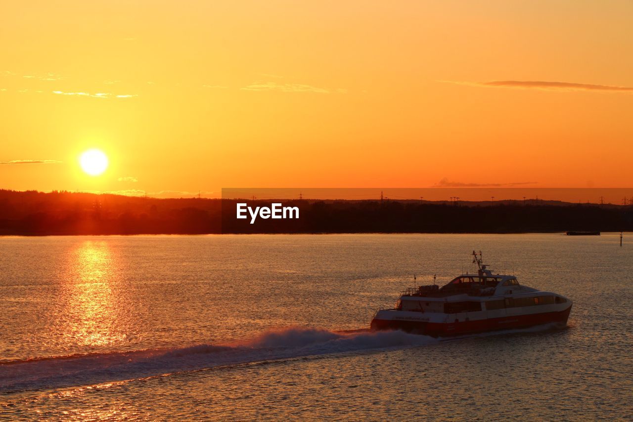 BOAT IN CALM SEA AGAINST ORANGE SKY