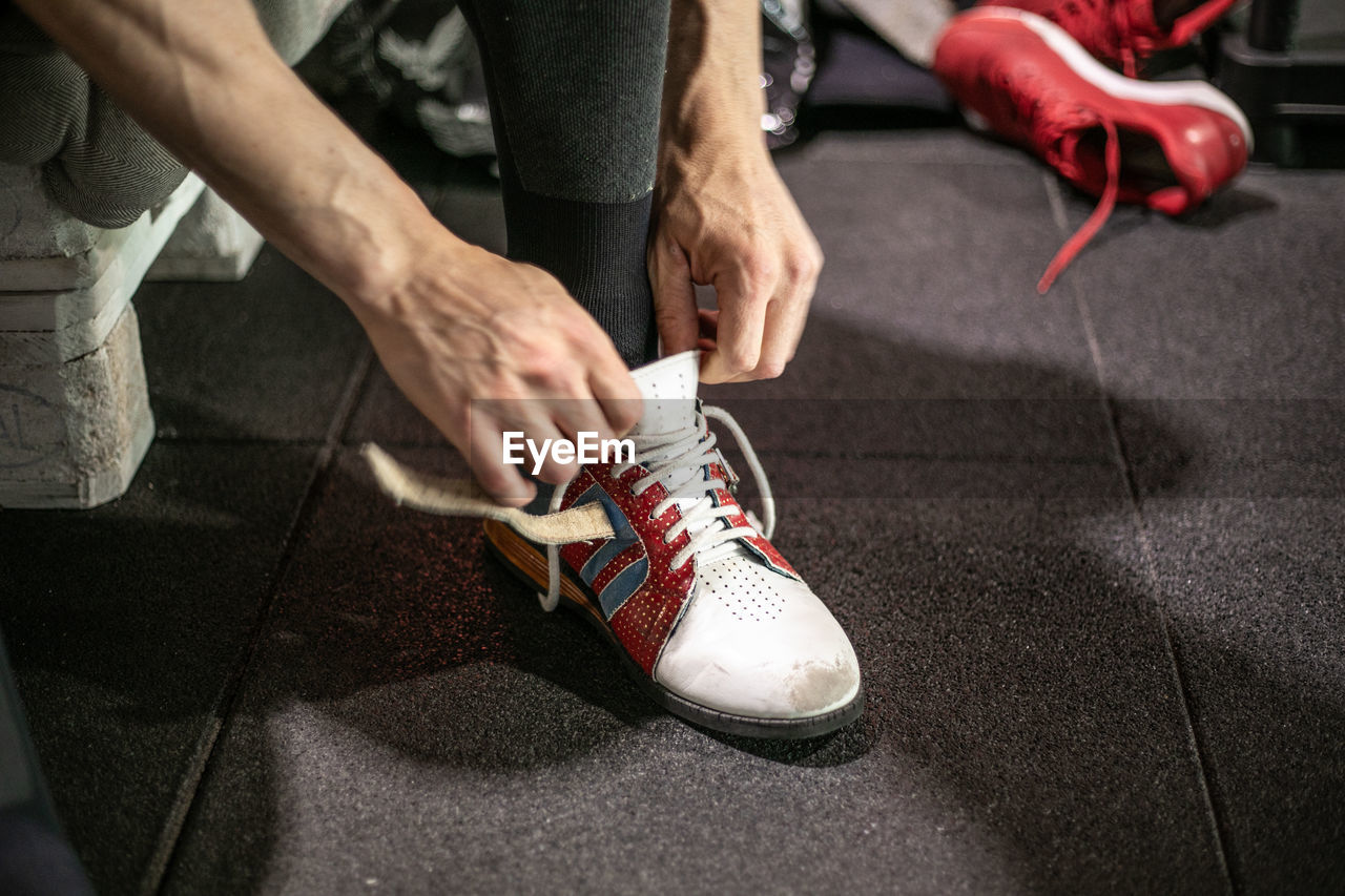 Cropped unrecognizable athletic male weightlifter putting on sport shoes before workout in modern gym