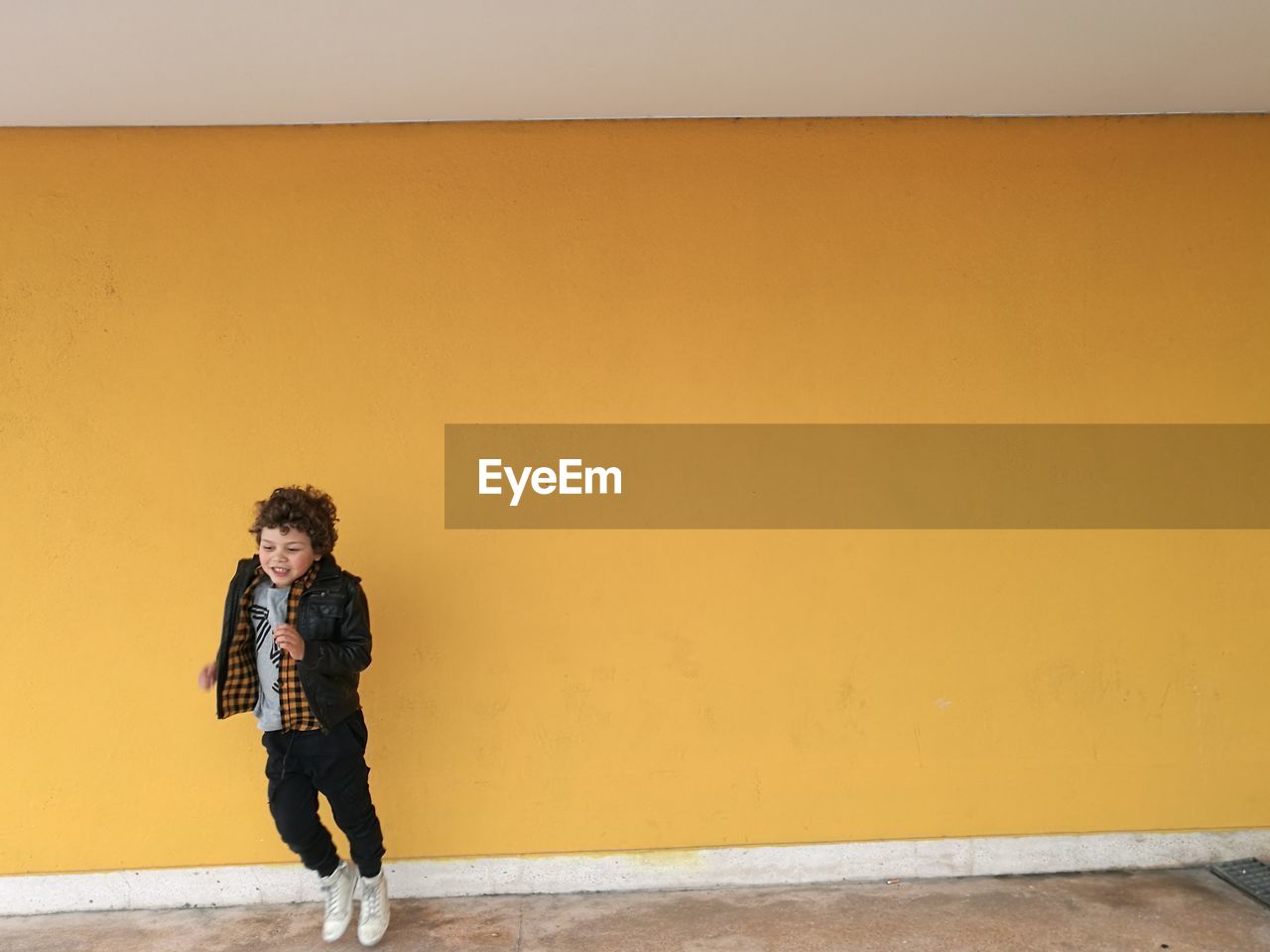 Full length of boy jumping against yellow wall