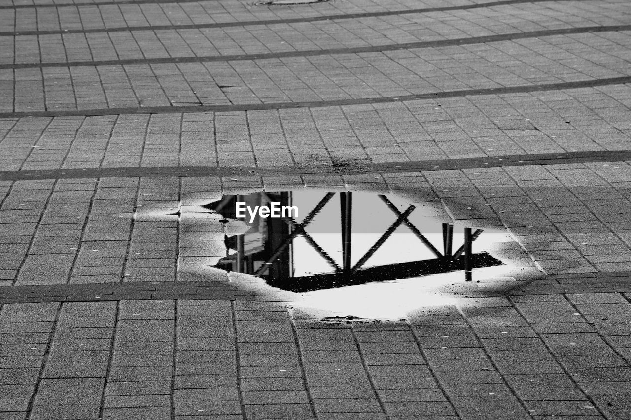 Built structure reflecting on puddle over cobbled street