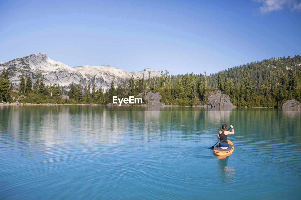 Attractive woman paddles stand up paddle board on blue lake.