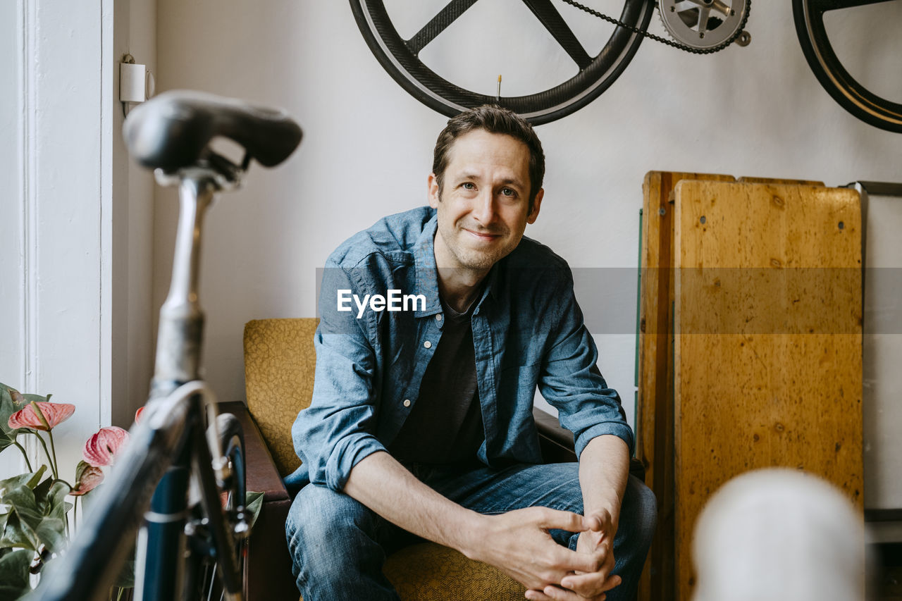 Portrait of smiling male owner sitting in bicycle shop