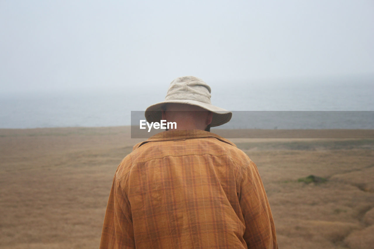 Rear view of man standing on land by sea against sky