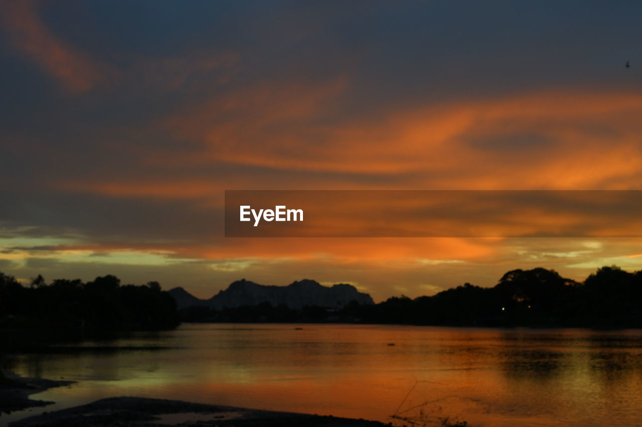 SCENIC VIEW OF LAKE BY SILHOUETTE MOUNTAINS AGAINST ORANGE SKY