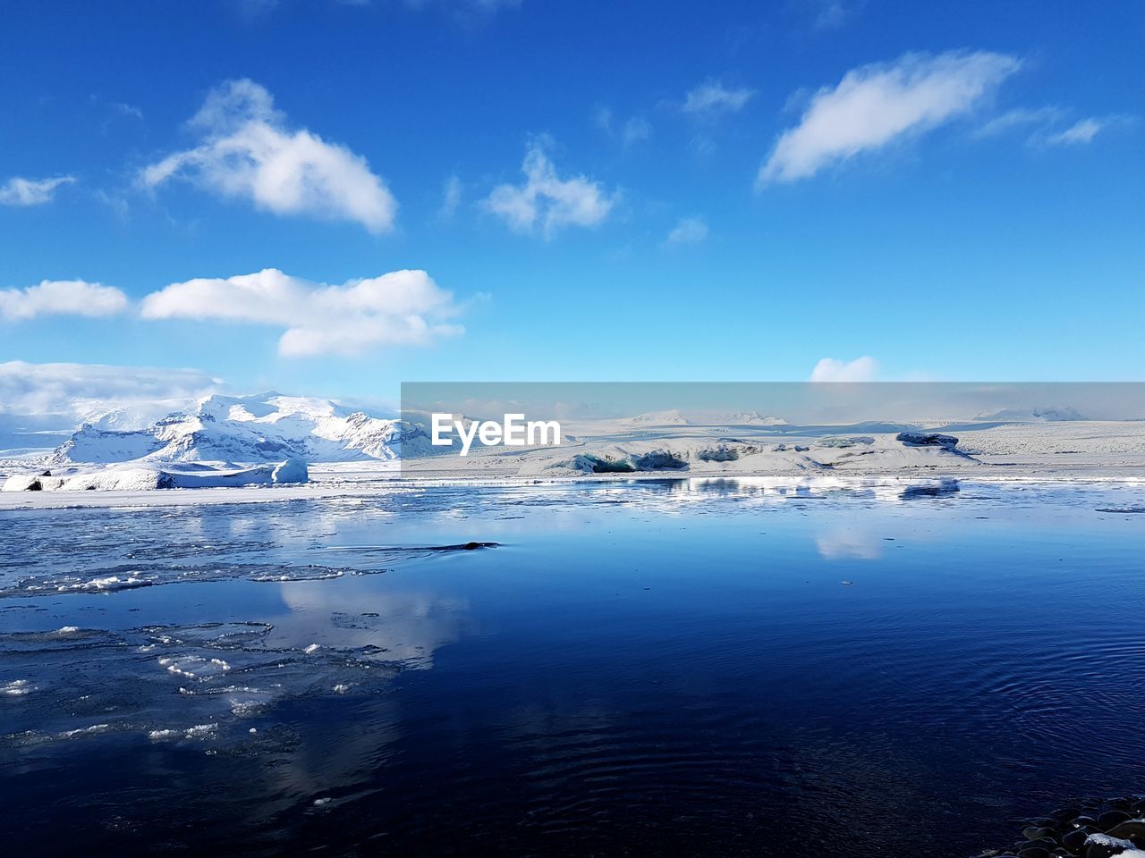 Scenic view of sea and snowcapped mountains against blue sky