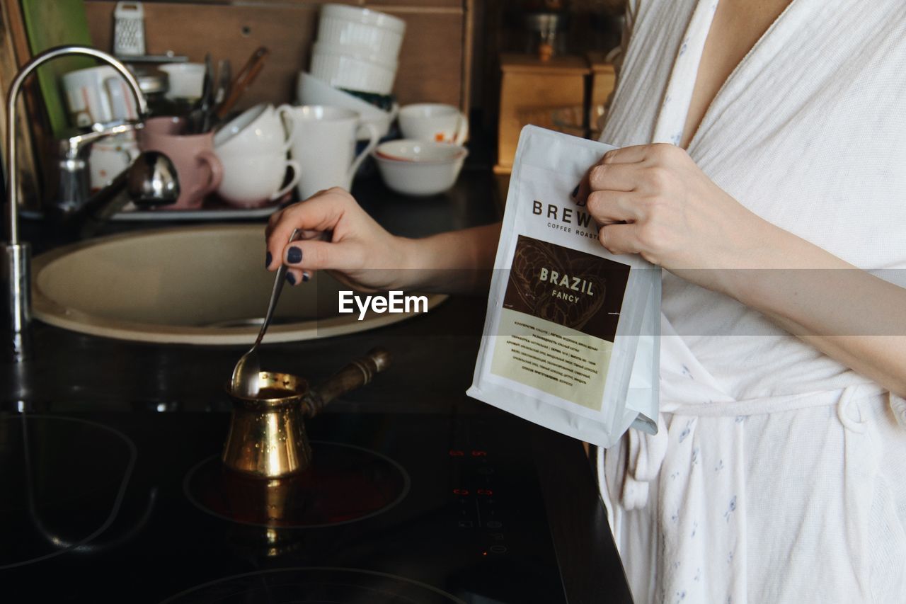 MIDSECTION OF WOMAN HOLDING FOOD IN KITCHEN