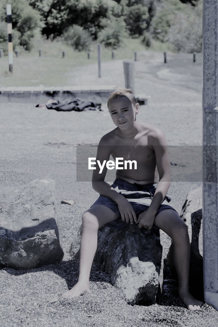 Full length of shirtless boy sitting on rock