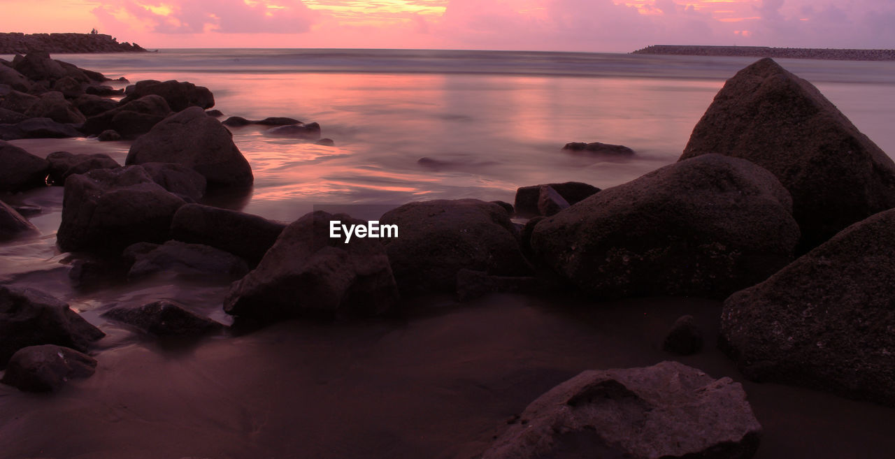 Rocks at sea shore against sky during sunset