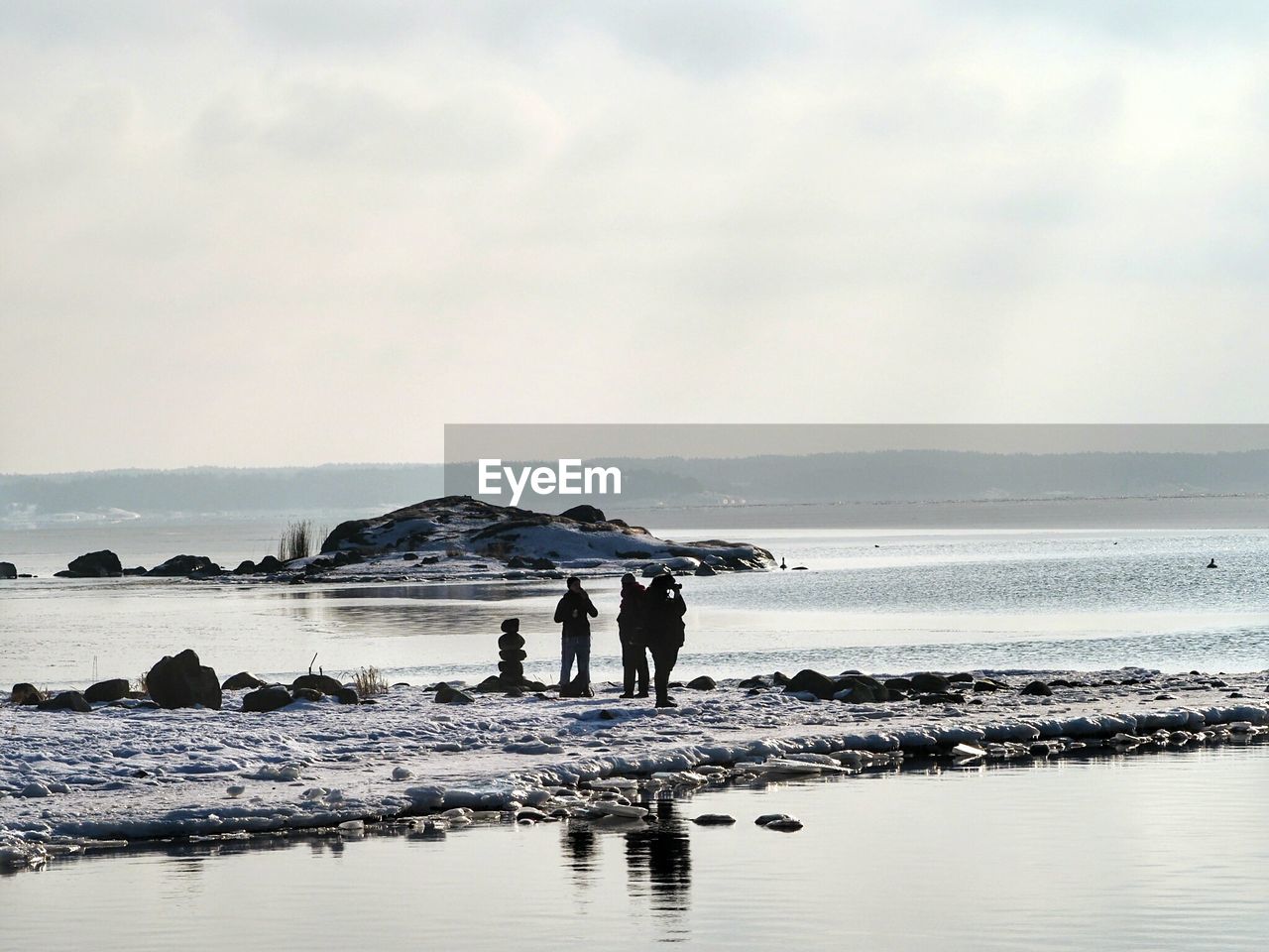 REAR VIEW OF MEN STANDING ON BEACH AGAINST SKY