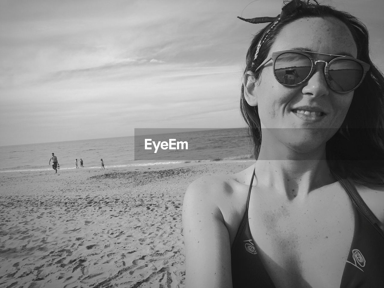 Smiling young woman wearing sunglasses at beach against sky