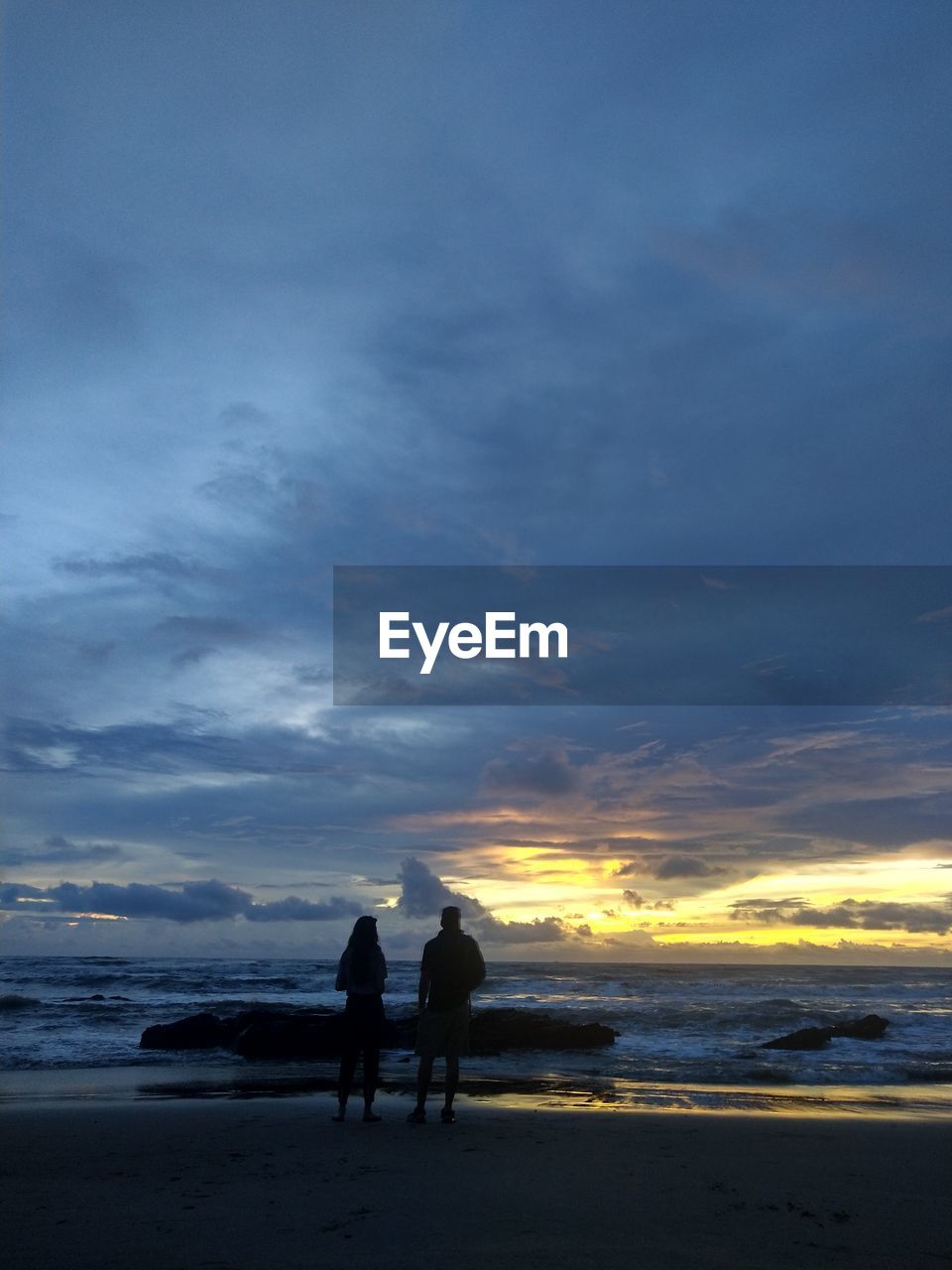 SILHOUETTE OF PEOPLE ON BEACH AGAINST SKY DURING SUNSET