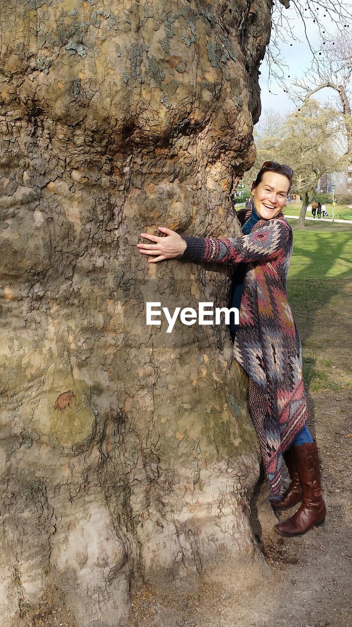 Portrait of woman standing with arm around tree