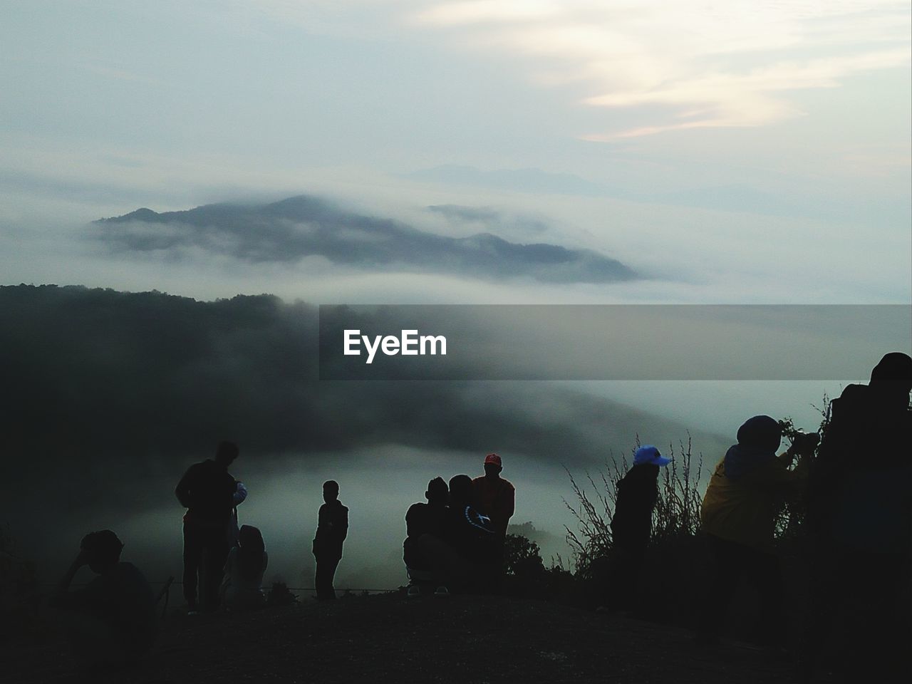 Silhouette people at mountains against cloudy sky