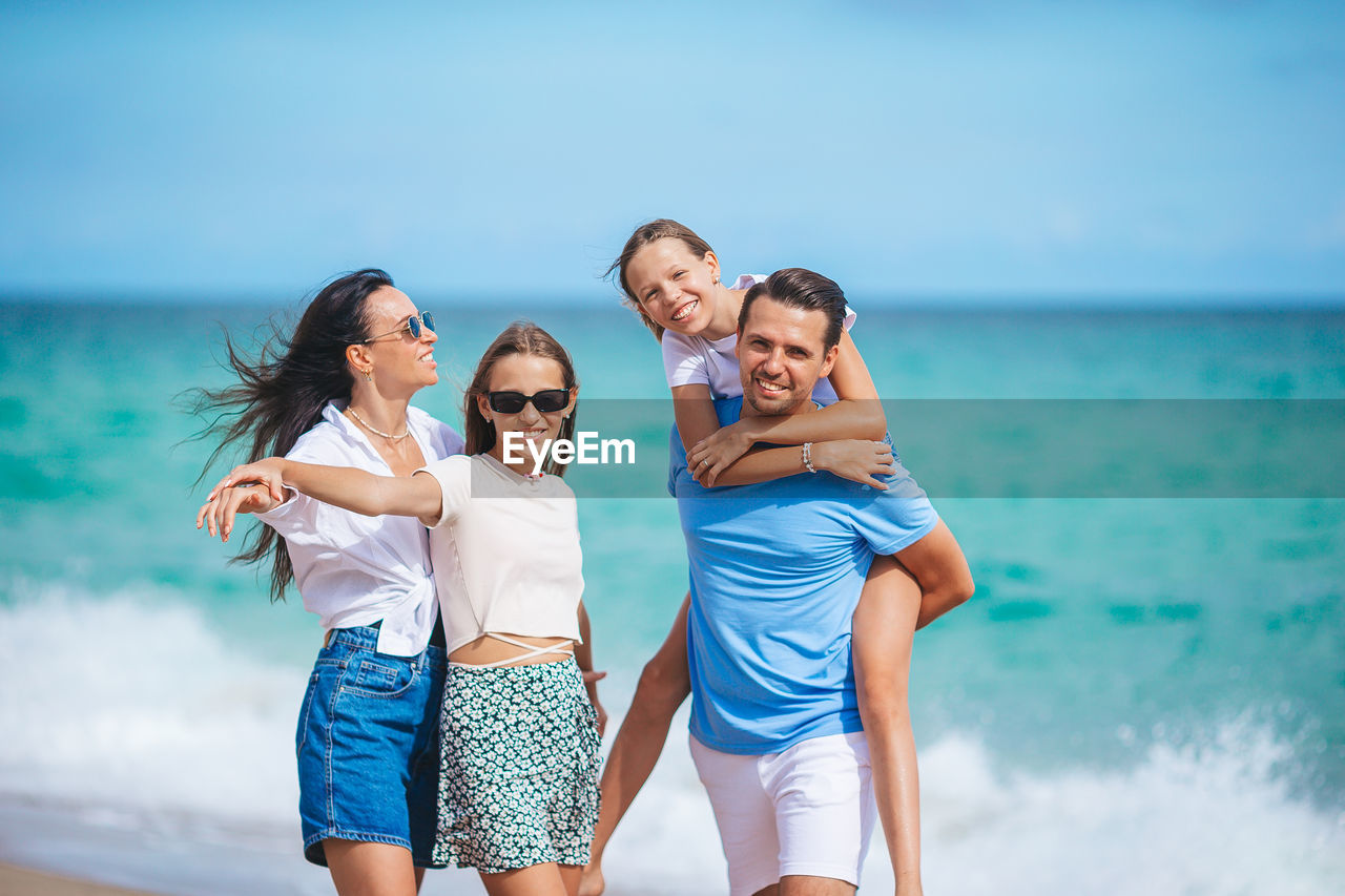 portrait of smiling friends standing at beach against sky