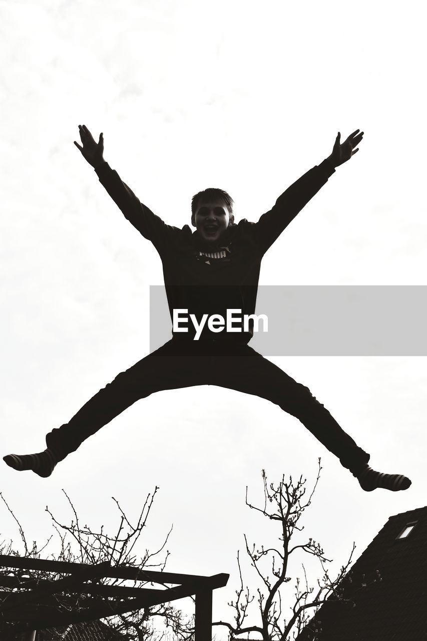 LOW ANGLE VIEW OF PERSON WITH ARMS RAISED AGAINST SKY