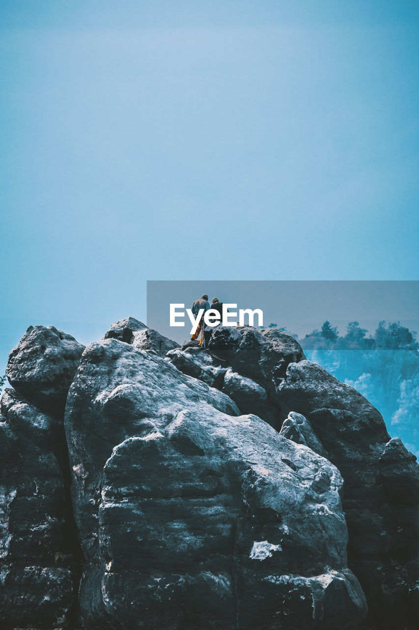 LOW ANGLE VIEW OF MAN STANDING ON ROCK AGAINST SKY