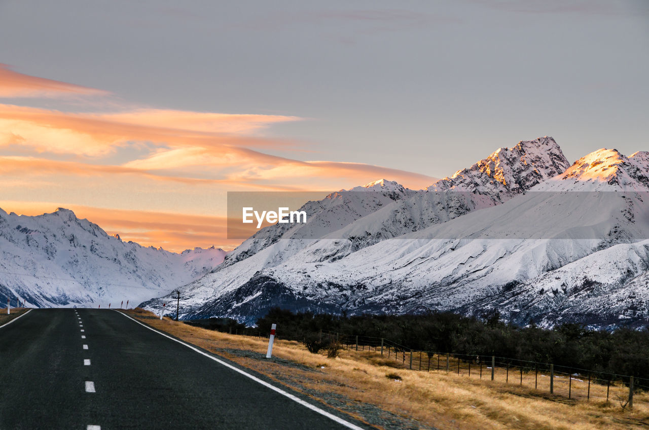 Road by mountains against sky during sunset