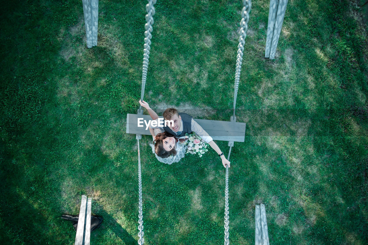 Portrait of bride and groom on swing at park