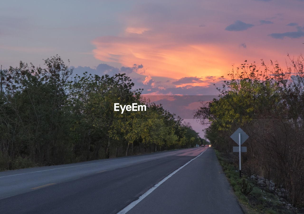 ROAD BY TREES AGAINST SKY AT SUNSET