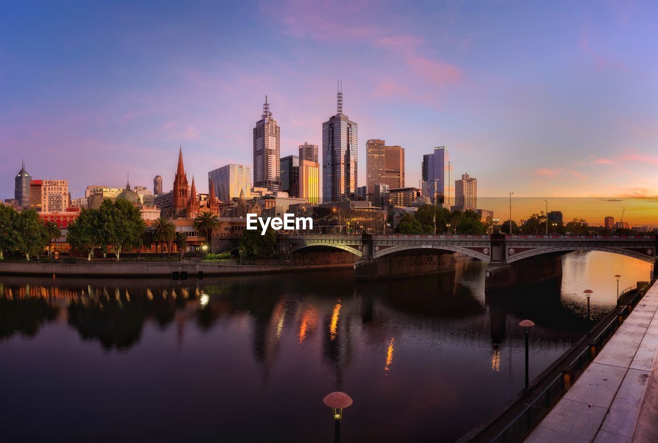 View of city at waterfront against cloudy sky