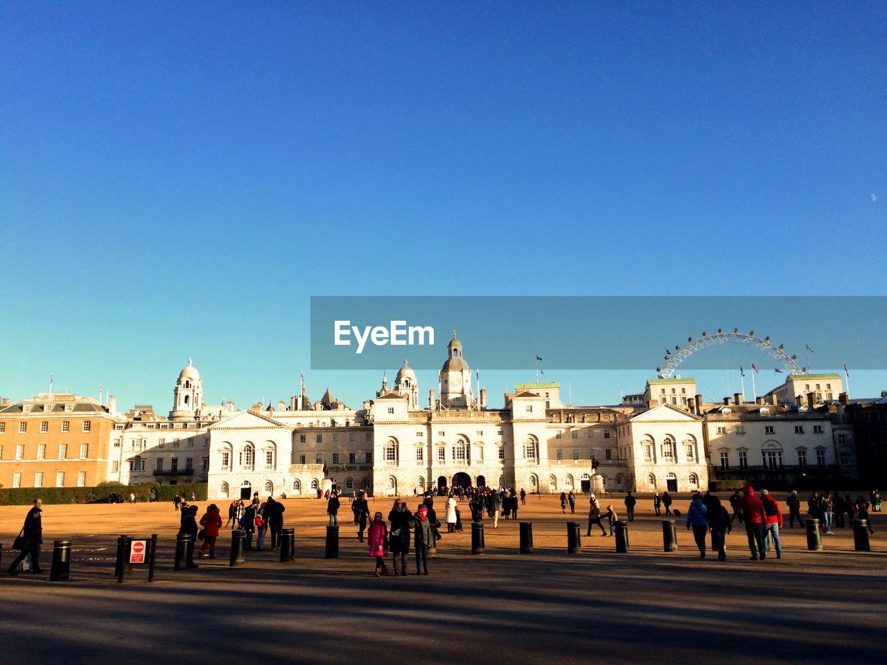 People walking by historic building against clear blue sky at st james park