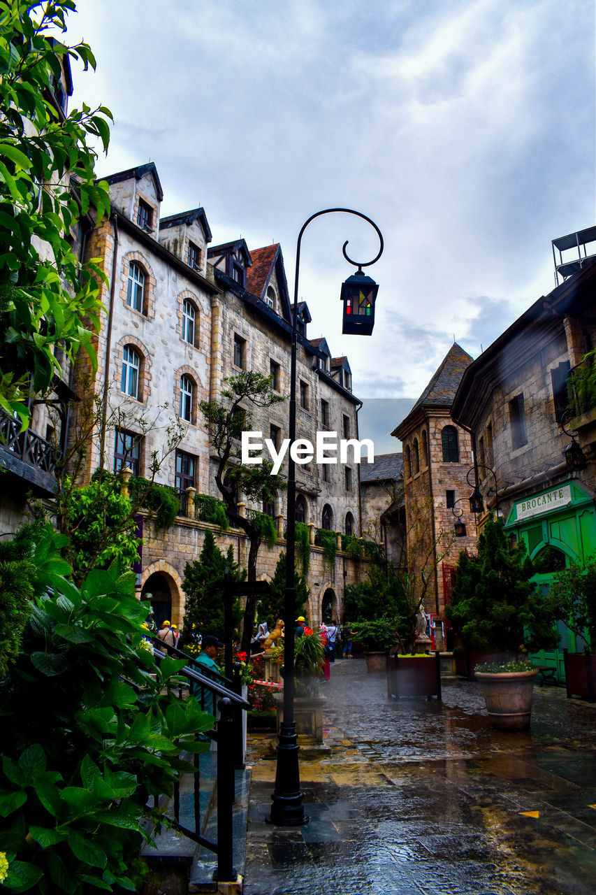 Wet street amidst buildings against sky