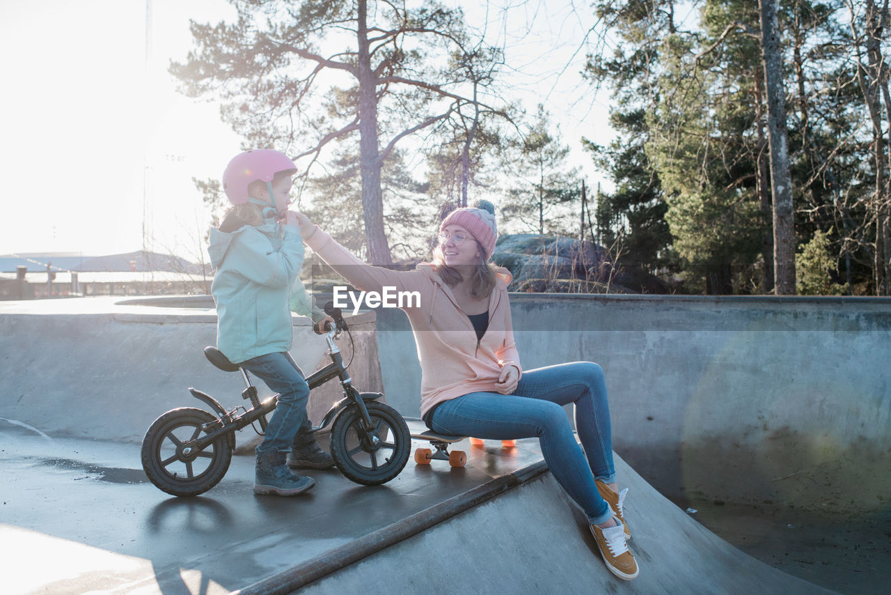 Mom helping her daughter with her helmet in a skatepark