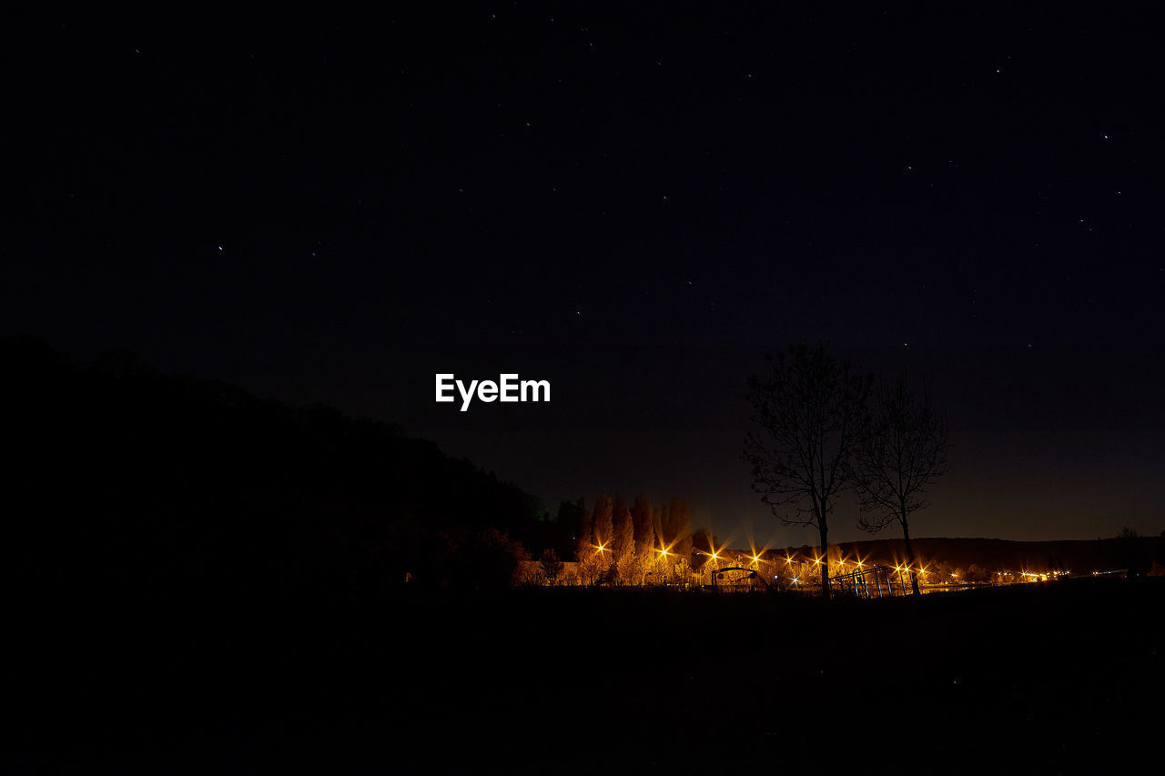 Silhouette trees on landscape against sky at night