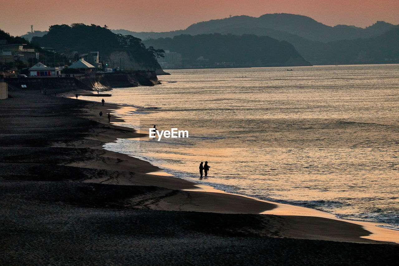 People on beach against sky during sunrise