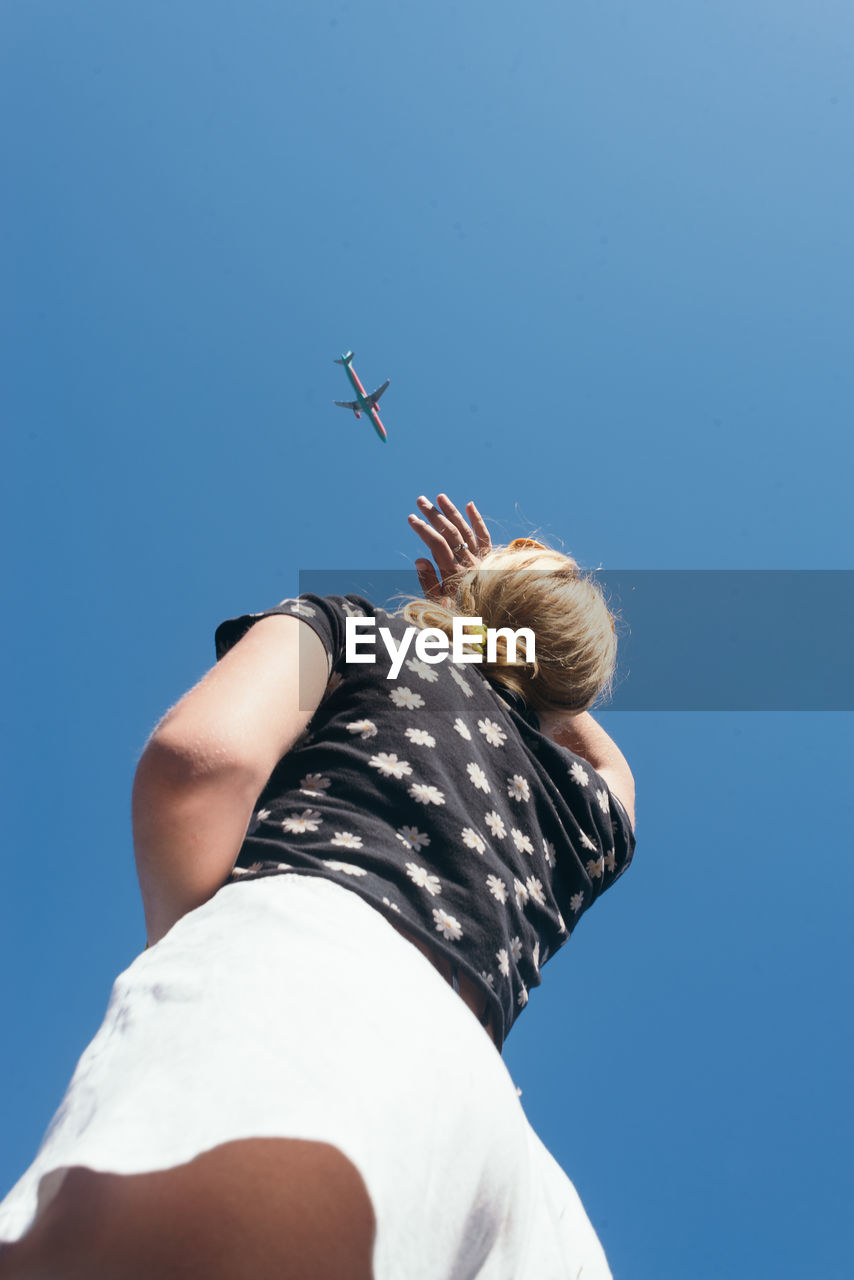 Low angle view of woman shielding eyes while looking at airplane