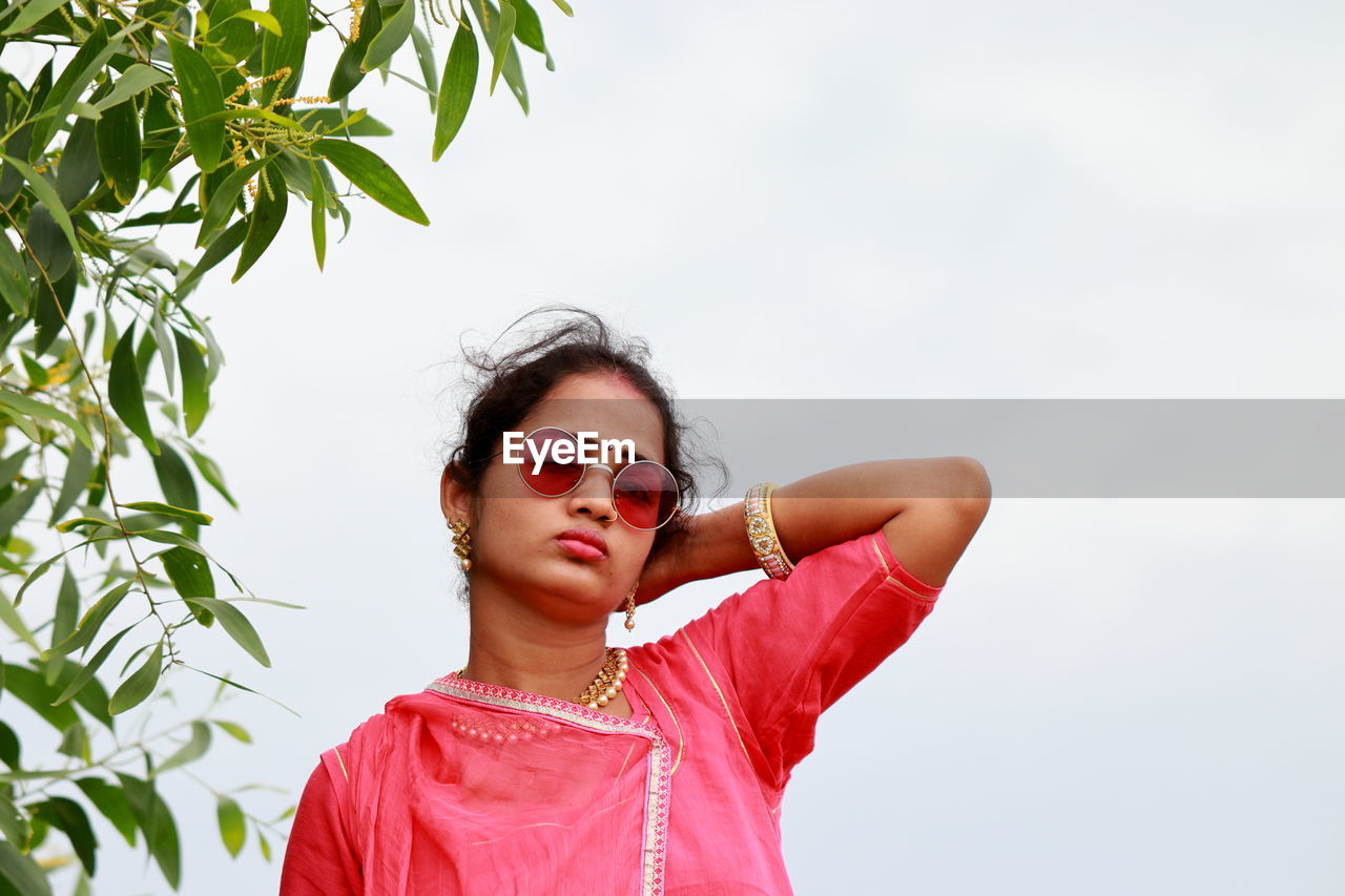 Portrait of young woman wearing sunglasses standing against sky