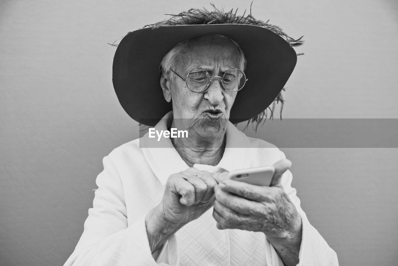 Close-up of senior woman using phone against gray background