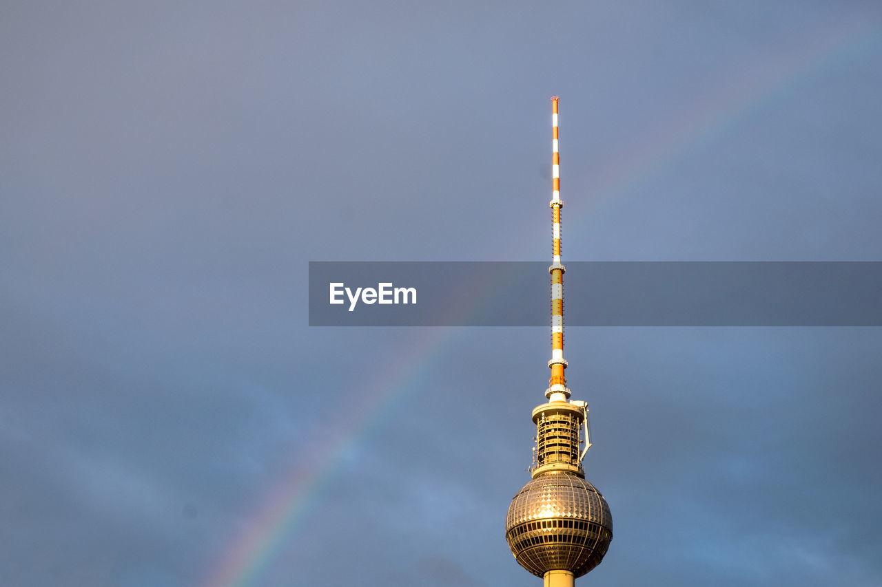 Low angle view of fernsehturm with rainbow against cloudy sky