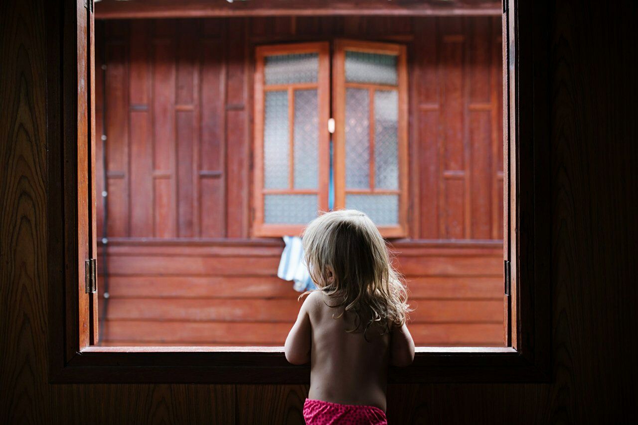 Rear view of young girl looking through window