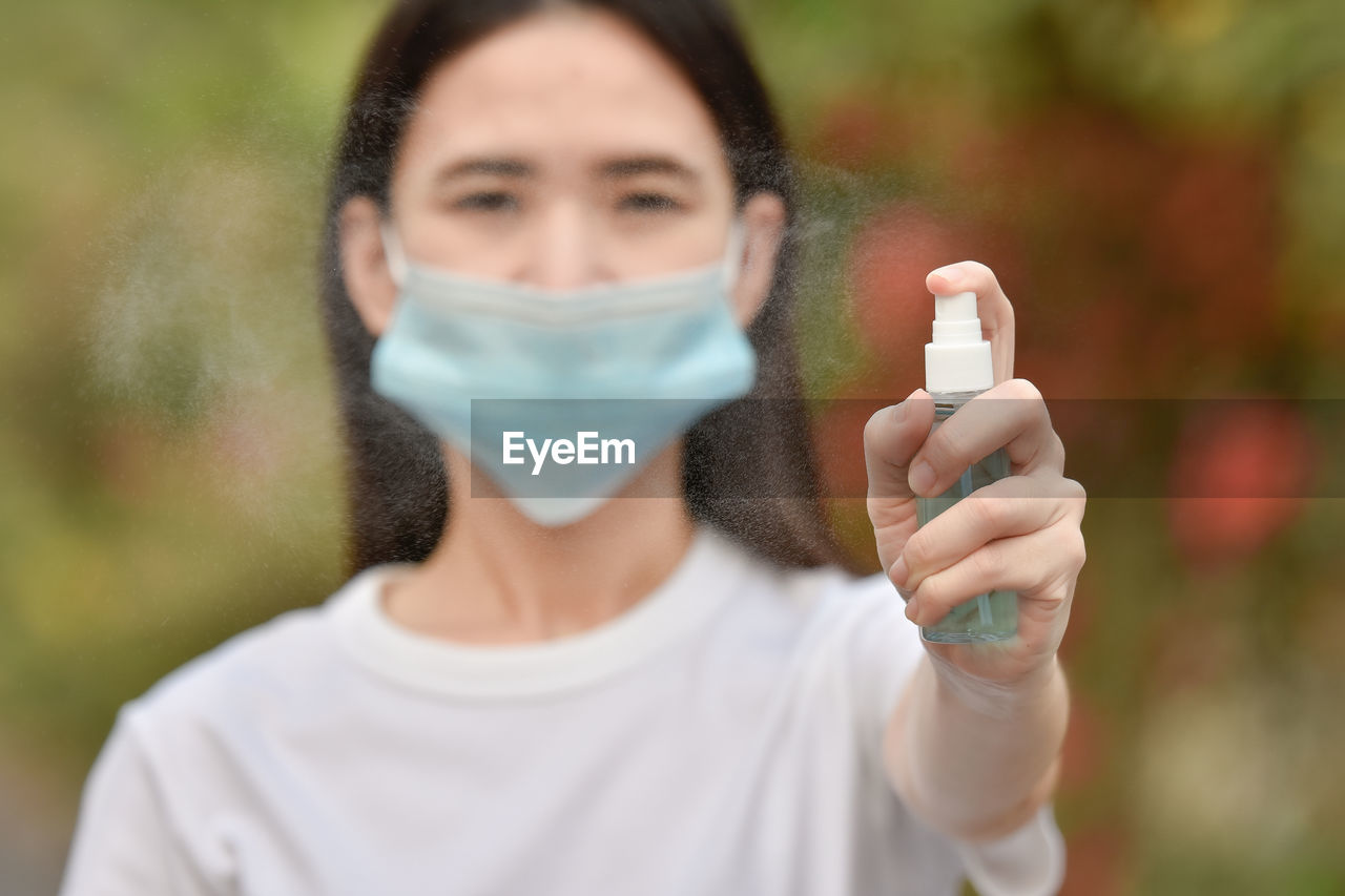 Portrait of young woman wearing mask holding hand sanitizer outdoors