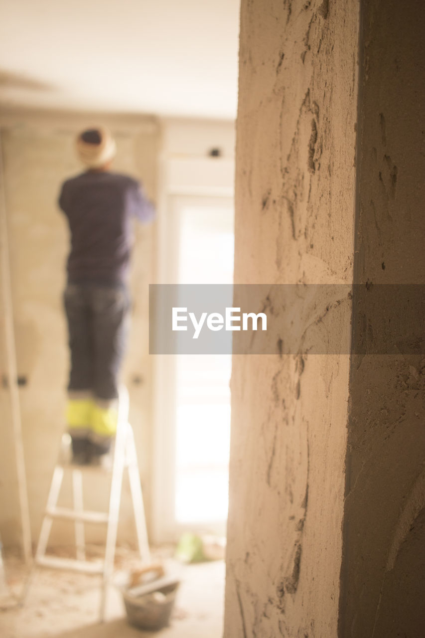 REAR VIEW OF MAN STANDING BY WALL