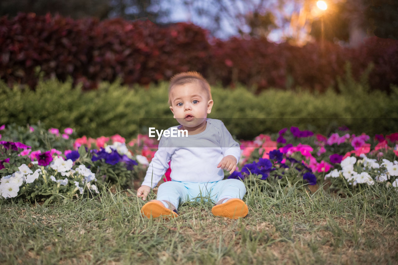 PORTRAIT OF CUTE BABY GIRL SITTING ON PLANT