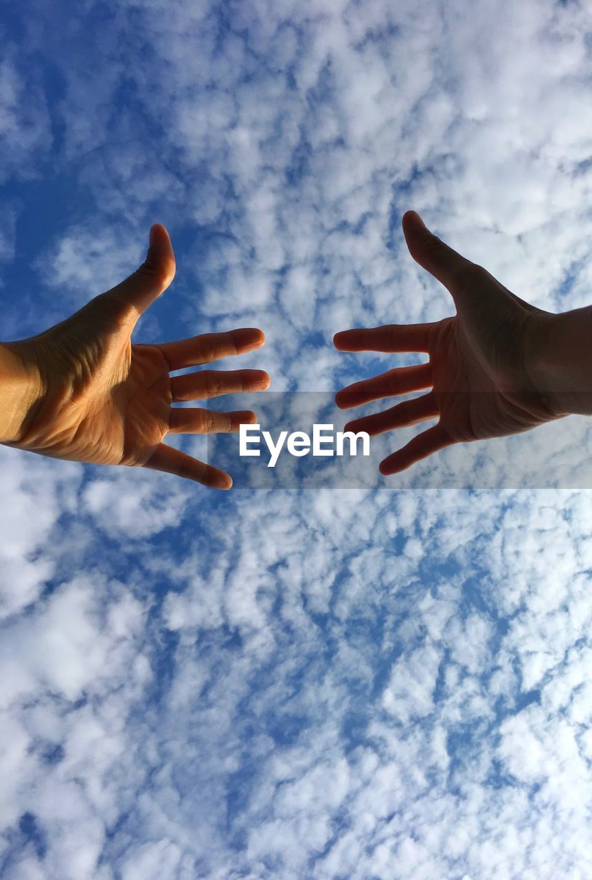 Cropped image of hands against cloudy sky