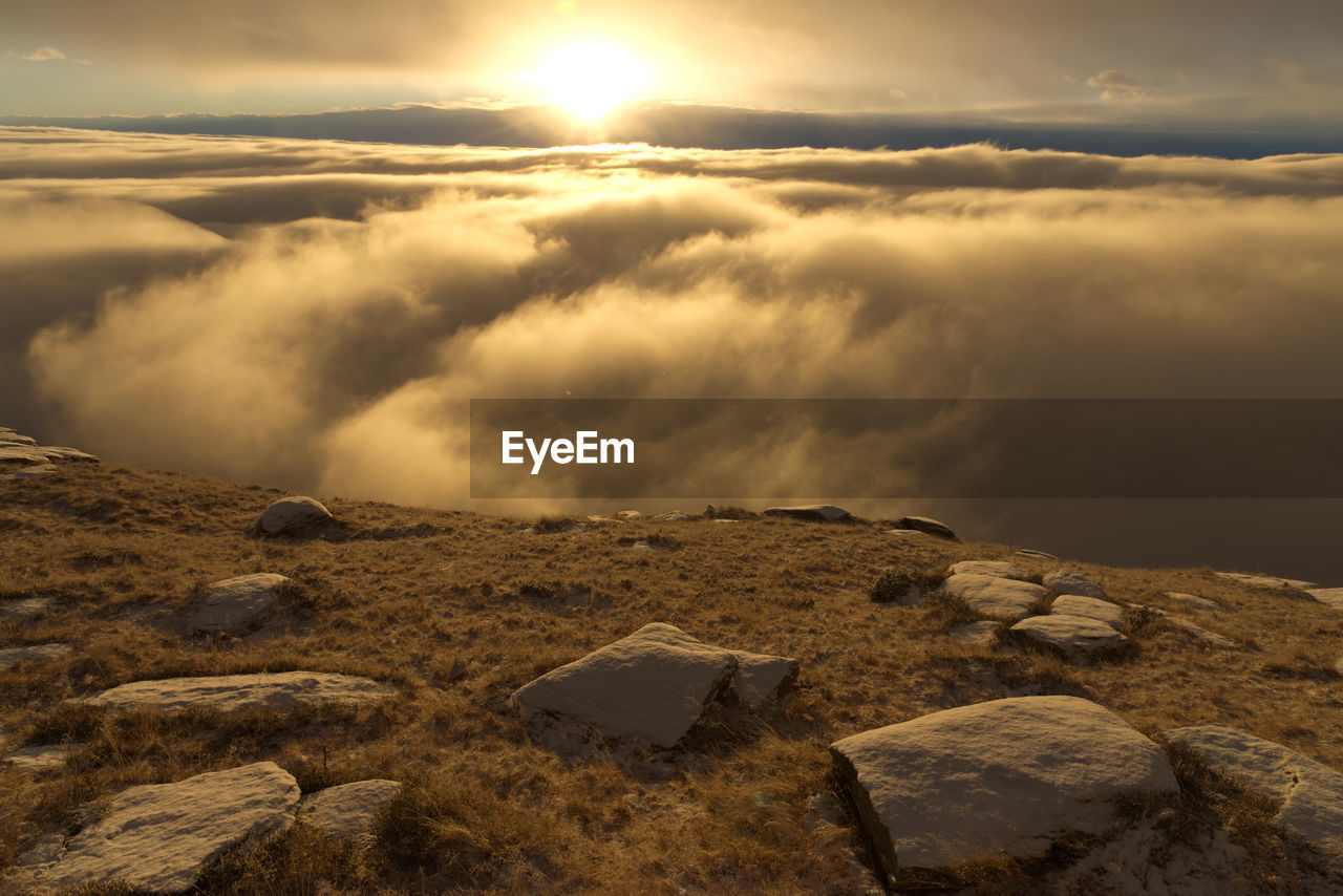 Scenic view of rocks and sea of clouds against sky during sunset