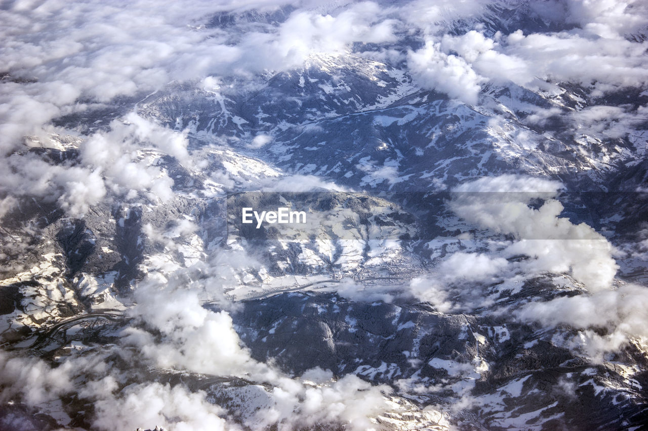 Aerial view of mountains against clouds during winter