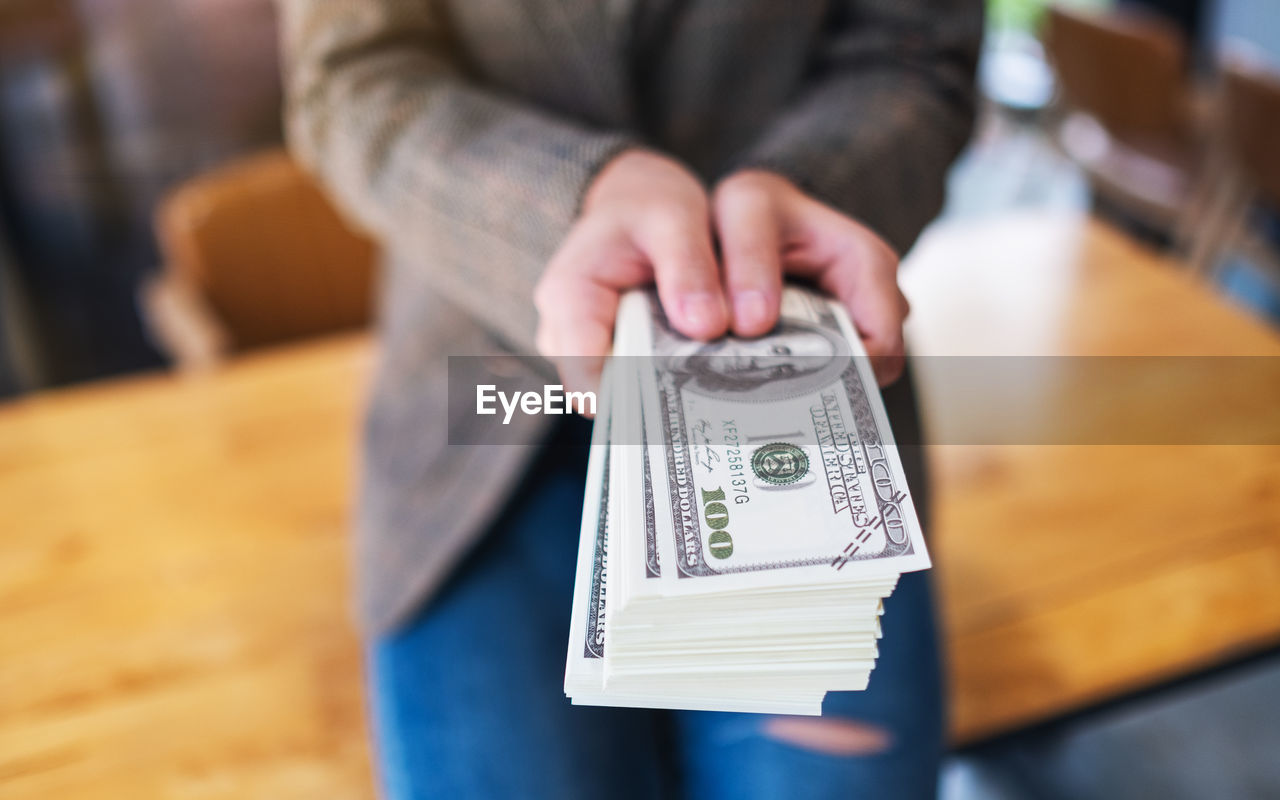 midsection of woman holding paper currency on table