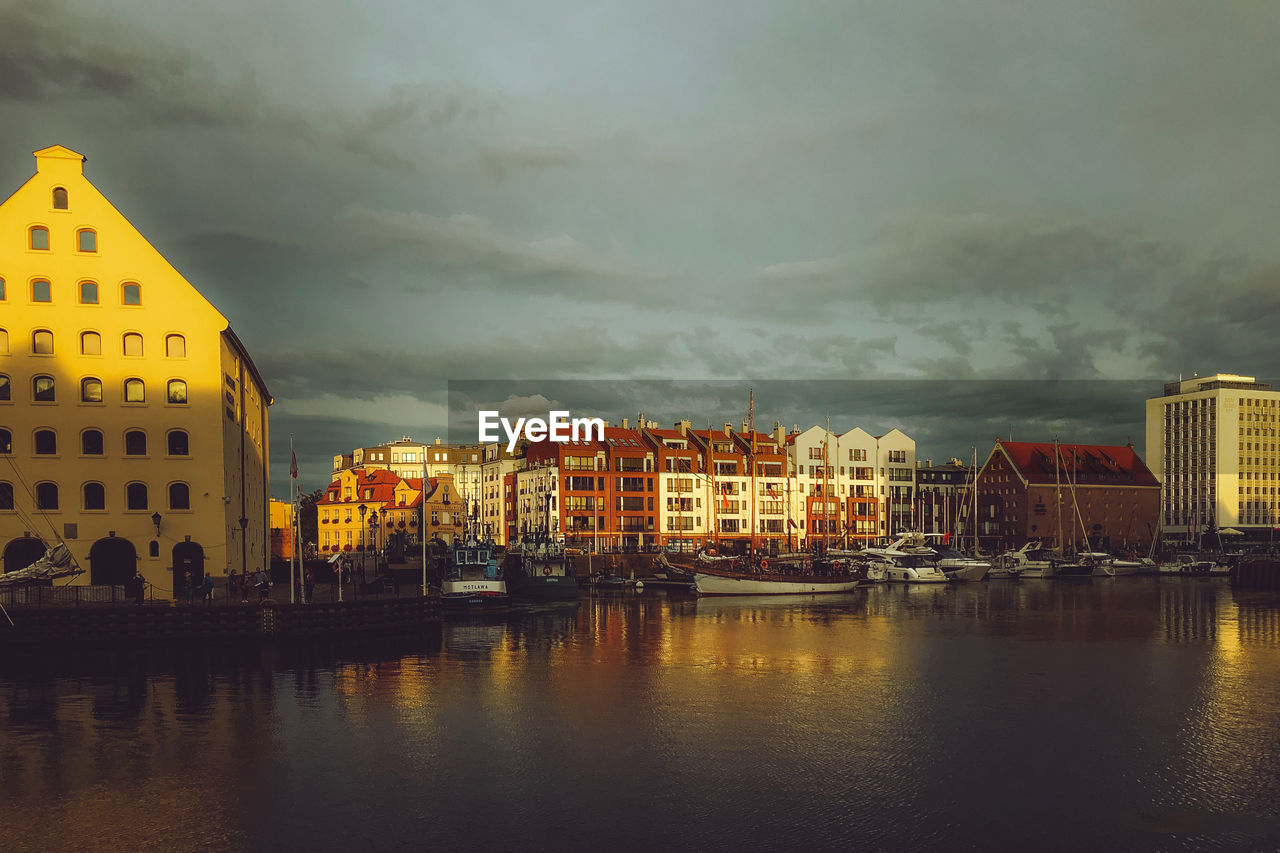 Buildings by river against sky in city