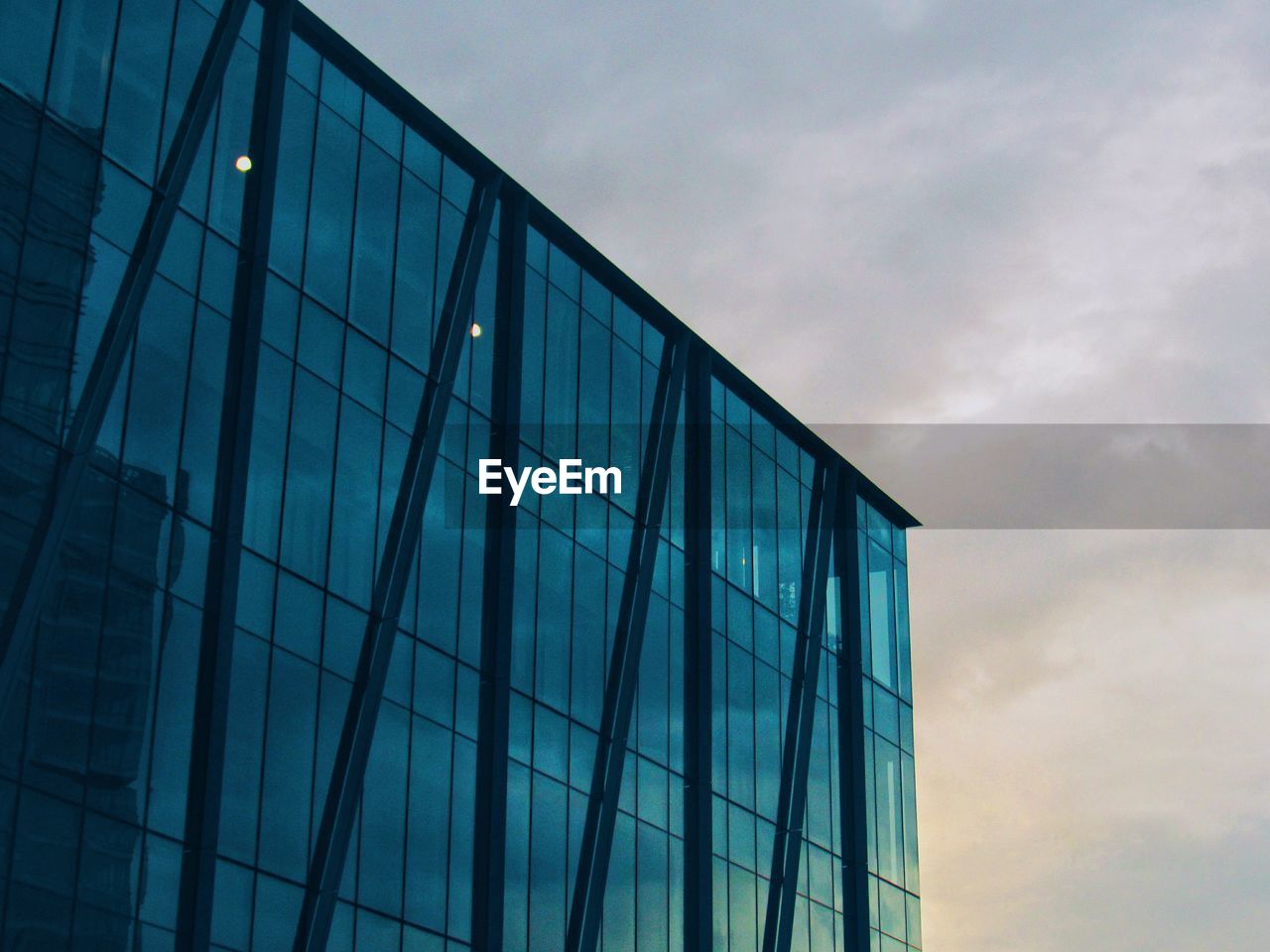 LOW ANGLE VIEW OF GLASS BUILDING AGAINST CLOUDY SKY