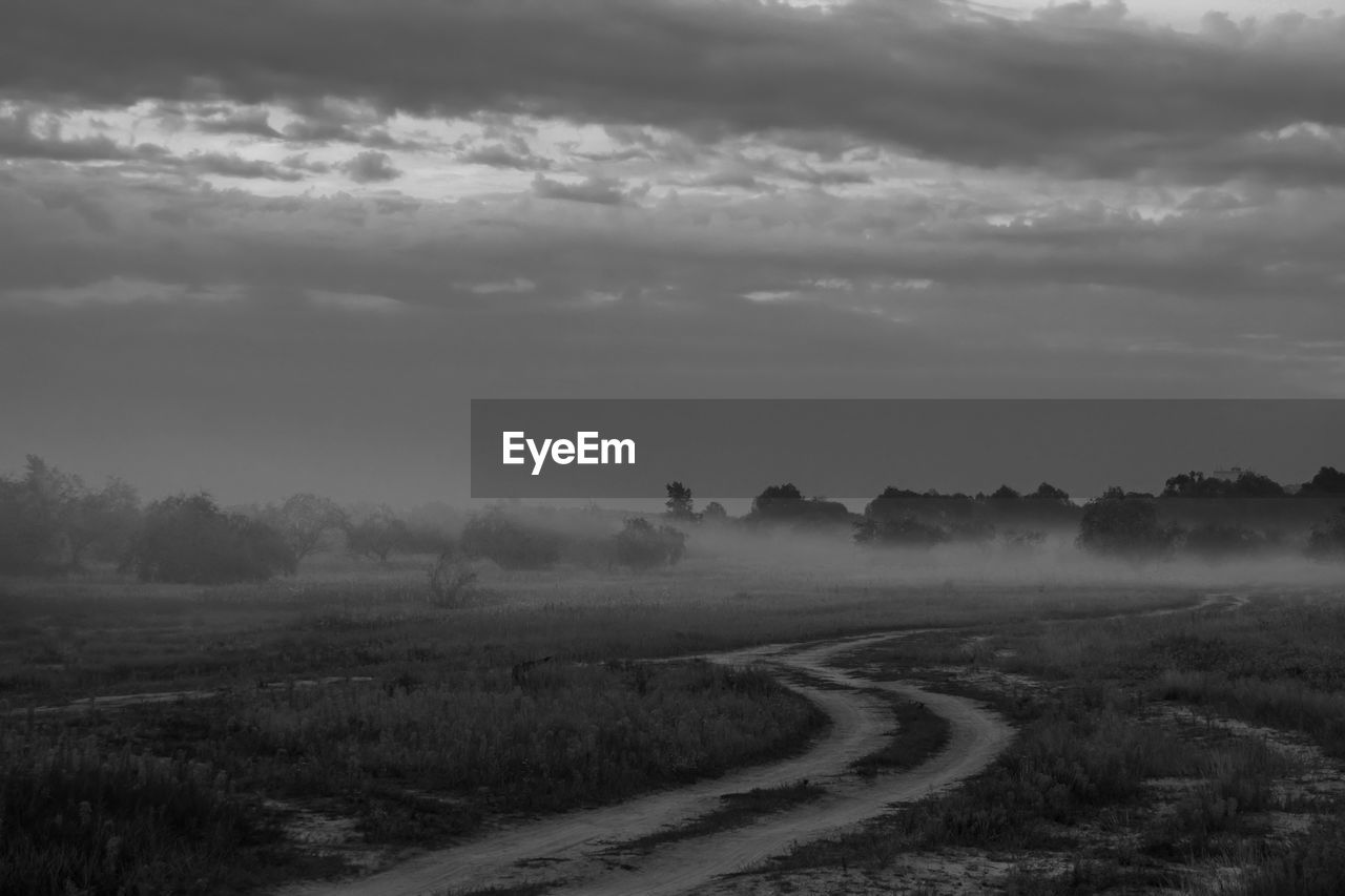 Footpath amidst field against cloudy sky