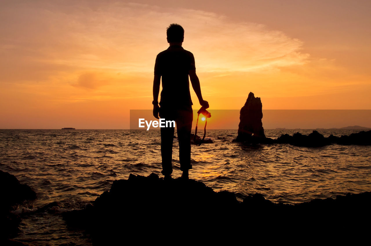 Silhouette of photographer standing on the rock at ocean