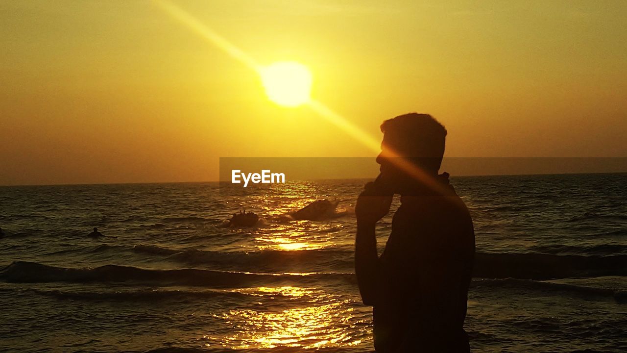 SILHOUETTE WOMAN STANDING ON SEA AGAINST SKY DURING SUNSET