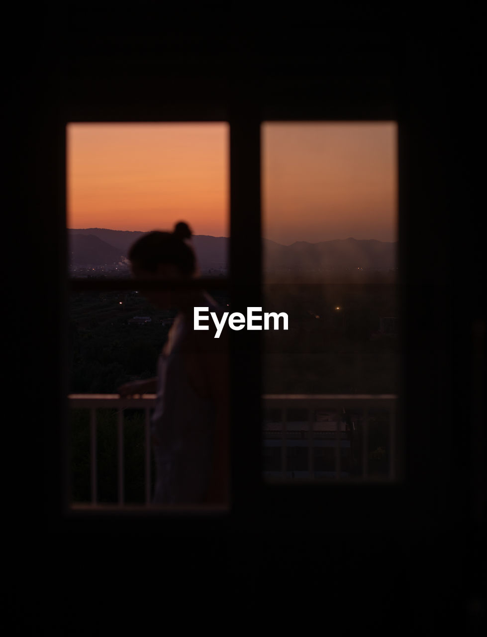 Side view of young faceless lady standing in a balcony with magnificent sunset on blurred background